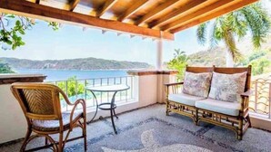 A covered outdoor seating area with a view of the sea, a wicker chair, a cushioned bench, and a small table. - ESPECTACULAR CASA EN ACAPULCO (Laredo)