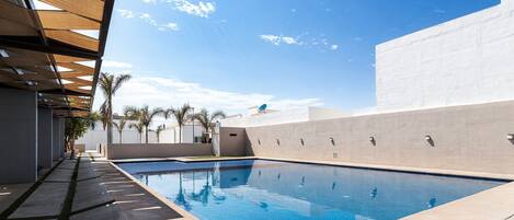 A swimming pool with a clear blue water surface, surrounded by a concrete deck and a pergola structure.