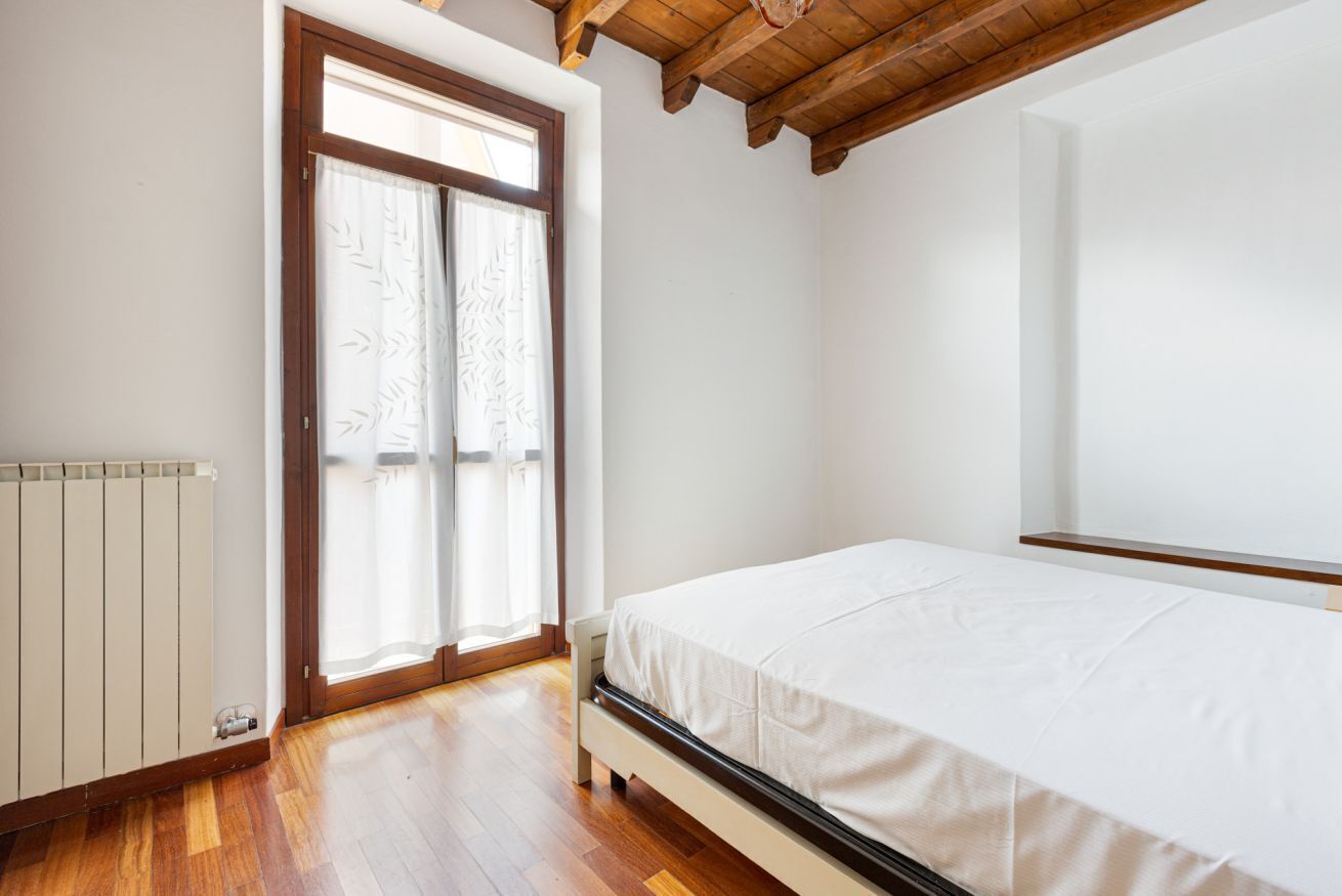 Une chambre avec un plancher en bois, un lit, un radiateur et une fenêtre avec un rideau.