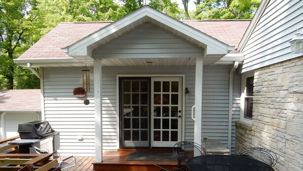 A covered patio with a grill, outdoor seating, and a door leading to a garage.