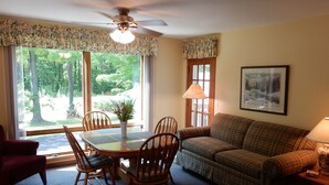 A cozy living room with a plaid sofa, wooden chairs, a dining table, and a ceiling fan.
