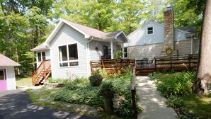 A two-story house with a stone chimney, a covered porch, and a wooden deck.