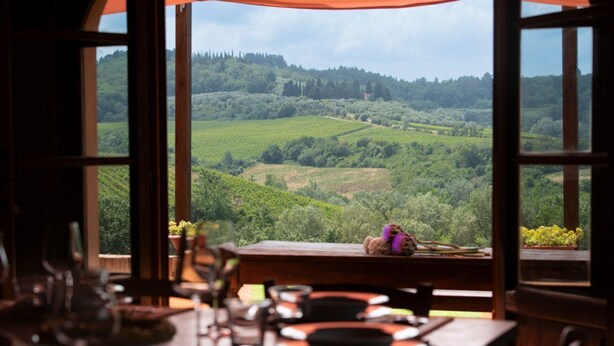 Un comedor con una mesa dispuesta para dos, vistas a un viñedo y una mesa de madera con un adorno pequeño.