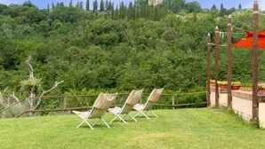 Zona verde con tres sillas de mimbre, una cerca de madera y vista a una colina con una torre.