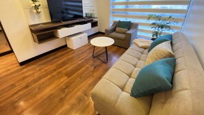 A modern living room with a flat-screen TV, a sofa, a chair, and a coffee table. - Great Location 2 Bedrooms 2,5 Bathrooms GYM Wifi Pool Jacuzzi GYM 24hr Security (Quito)