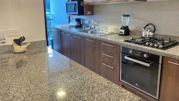 A modern kitchen with granite countertops, wooden cabinets, a built-in microwave, a kettle, a blender, and a stove. - Great Location 2 Bedrooms 2,5 Bathrooms GYM Wifi Pool Jacuzzi GYM 24hr Security (Quito)
