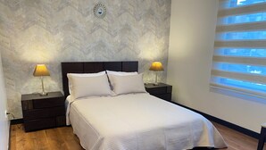 A neatly made bed with a textured white bedspread, two bedside lamps, a dark wooden nightstand, and a wall with a geometric pattern. - Great Location 2 Bedrooms 2,5 Bathrooms GYM Wifi Pool Jacuzzi GYM 24hr Security (Quito)
