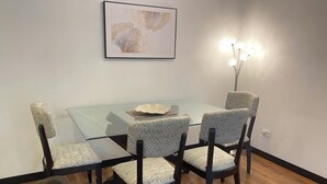 A dining area with a glass table surrounded by four patterned chairs, a framed artwork on the wall, and a floor lamp. - Great Location 2 Bedrooms 2,5 Bathrooms GYM Wifi Pool Jacuzzi GYM 24hr Security (Quito)