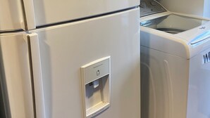 A compact kitchen with a white refrigerator, a built-in washing machine, and wooden cabinets. - Great Location 2 Bedrooms 2,5 Bathrooms GYM Wifi Pool Jacuzzi GYM 24hr Security (Quito)