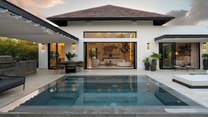 Ett modernt hus med en swimmingpool, utomhusmöbler och ett stort fönster med en dekorativ väggdekoration.