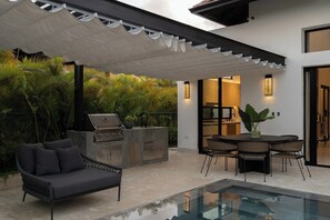 Une terrasse extérieure avec un barbecue, des sièges et une piscine.