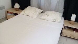 Ein ordentlich bezogenes Bett mit weißer Bettwäsche und zwei Kissen, begleitet von zwei Nachttischen mit Lampen, in einem Raum mit schwarzem Vorhang im Hintergrund.