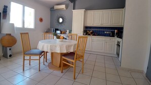 Ein Essbereich mit einem runden Tisch und vier Stühlen, eine Küche mit weißen Schränken und eine Decke mit sichtbaren Holzbalken.