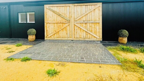 A building with a large wooden garage door, a metal roof, and a paved entrance area with potted plants.