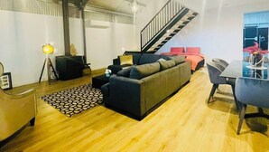 A modern living room with a sofa, a dining table, and a staircase.