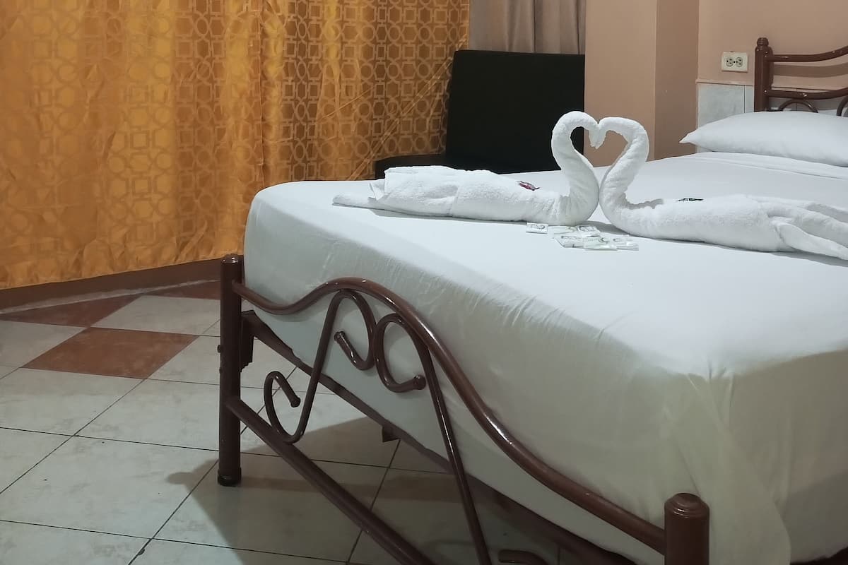 Una camera d'albergo con un letto, una televisione e una finestra con tende.