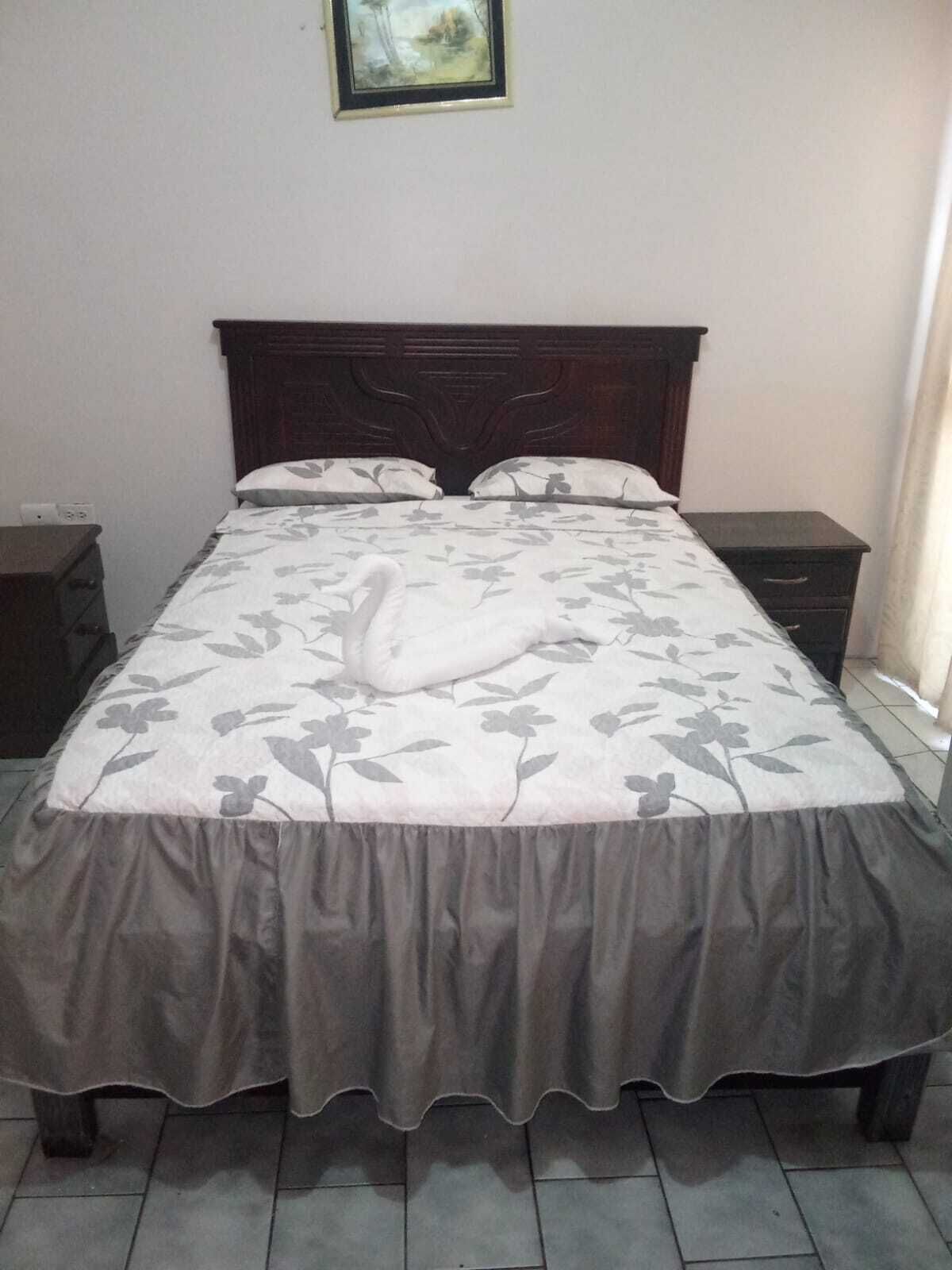 Een netjes opgemaakt bed met een bloemenbedekking en een decoratief zwaan kussen.