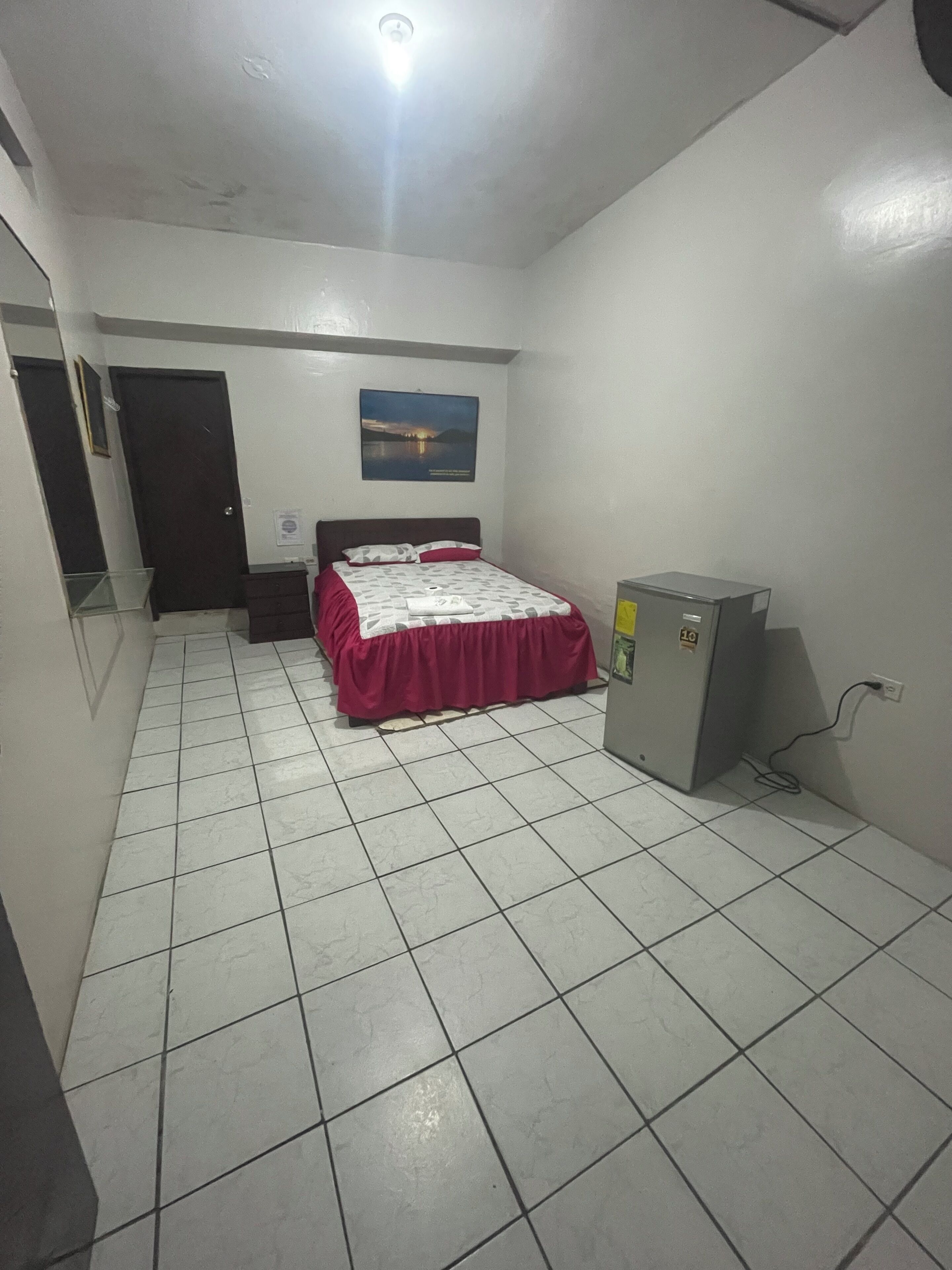 A bedroom with a bed, a dresser, a small cabinet, and a poster on the wall.