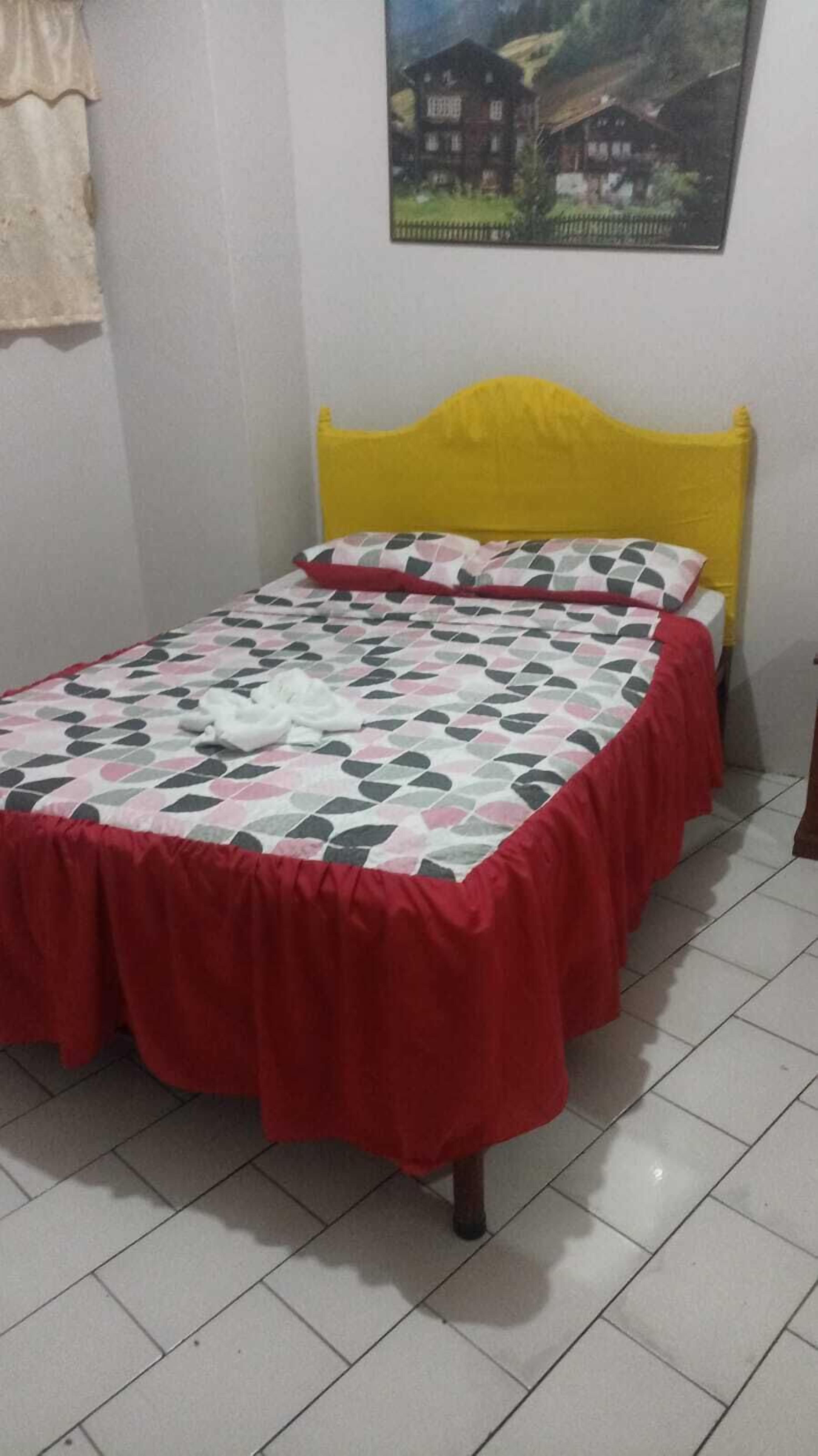 A bed with a yellow headboard, a red bedspread, and a patterned pillow.