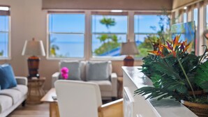 Un salon moderne comprenant un canapé, des fauteuils, une table basse et une grande fenêtre donnant sur l’océan.