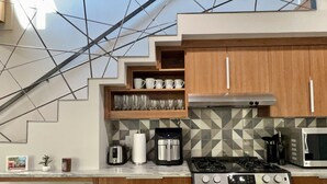 Une cuisine moderne équipée d’une cuisinière à gaz, d’un four à micro-ondes et d’une machine à café. Les meubles de rangement sont en bois et le mur derrière l’évier est recouvert de carreaux.