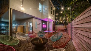 Une terrasse extérieure agrémentée de chaises en osier aux couleurs vives, d’un foyer et de guirlandes lumineuses.