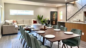 Un espace de salle à manger moderne, avec une longue table dressée pour six personnes, entourée de chaises recouvertes d’un tissu vert.