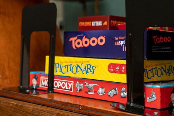 A collection of board games including Monopoly, Taboo, and Pictionary, stacked on a wooden surface. - Modern DT Retreat w/ Hot Tub King Bed Fast Wi-Fi
(Austin)