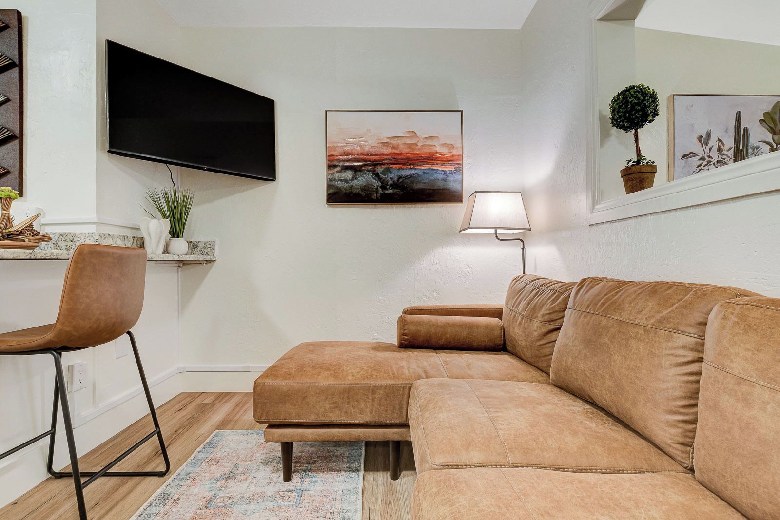 A modern living room with a sectional sofa, a flat-screen TV, a painting, a lamp, and a small potted plant.