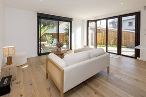 Una sala moderna con un sofá, una mesa redonda de madera y un pouf blanco.