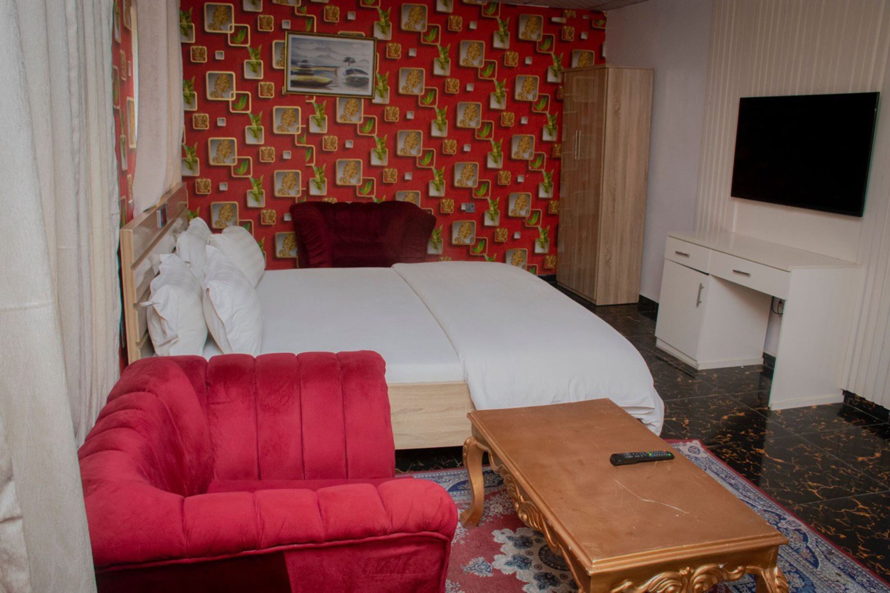 A hotel room with a bed, a red sofa, a wooden coffee table, a TV, and a wardrobe.