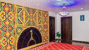 A hallway with a red tiled floor, a decorative wall with geometric patterns, a peacock design, and a chandelier. - Zaytun Hotel Kano (Kano)