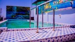 A swimming pool with tiled steps and metal railings, surrounded by a mural depicting a coastal scene. - Zaytun Hotel Kano (Kano)
