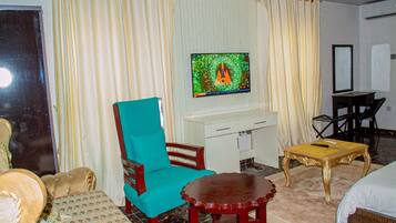 A hotel room with a teal armchair, a wooden table, a TV on the wall, and a bed.