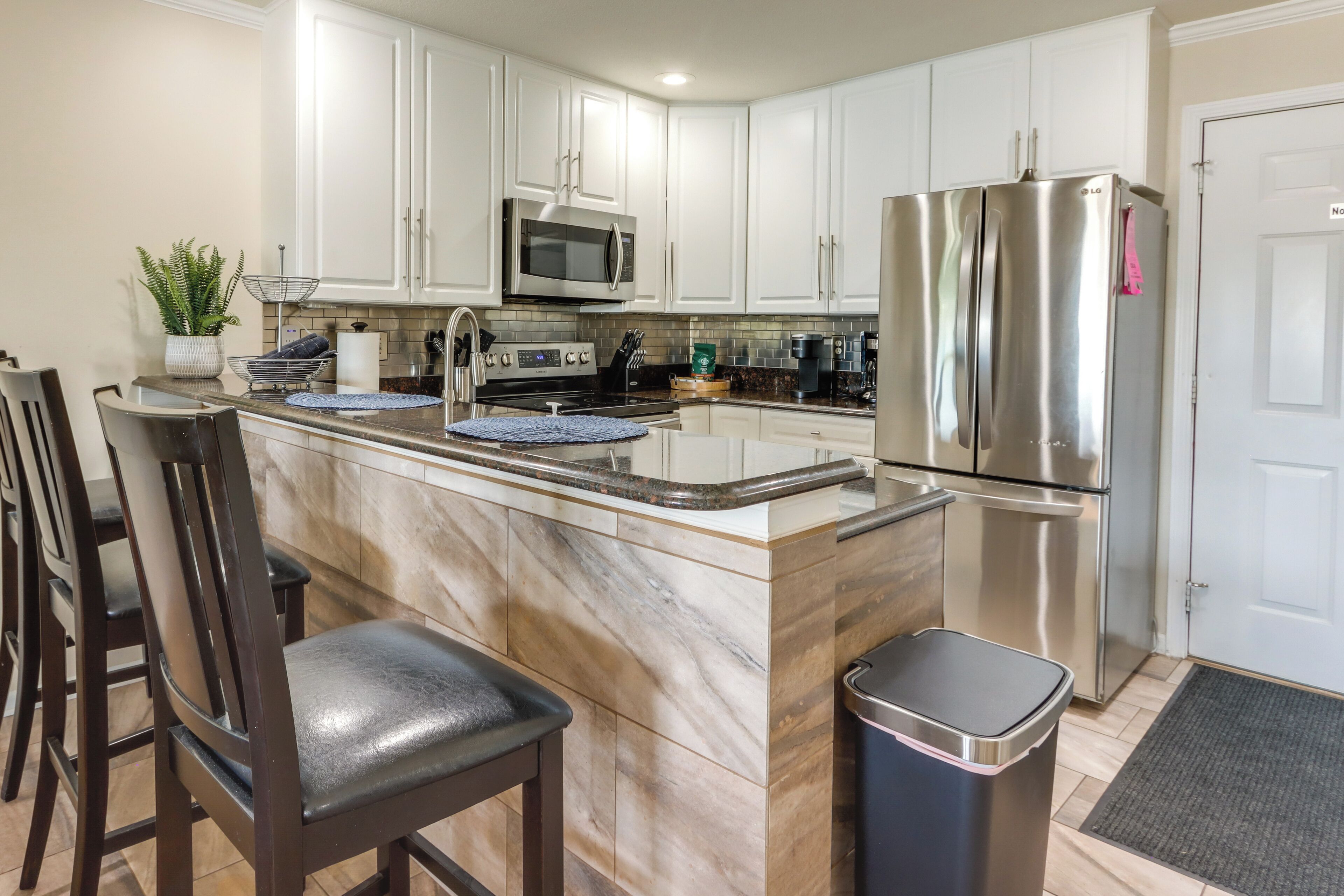 A kitchen with white cabinets, stainless steel appliances, a marble island, and a trash can.