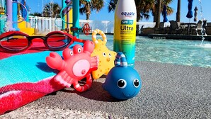 En strandscene med en pool, farverige parasoller og en solcremeflaske mærket SPF 70 Ultra.