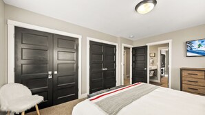A bedroom with a large bed, a white chair, and three dark doors. - Walk to Main Street, Ontario Adventures, Two Homes Combined  - 6 BR, 2 Private Decks with Hot Tubs (Park City)