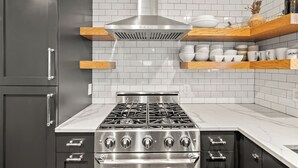 A kitchen with a stainless steel stove, dark cabinets, white tiled backsplash, and wooden shelves with dishes. - Walk to Main Street, Ontario Adventures, Two Homes Combined  - 6 BR, 2 Private Decks with Hot Tubs (Park City)