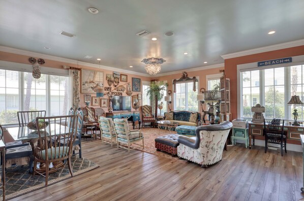 A spacious living room with hardwood floors, a chandelier, and a large window with a view of the beach.