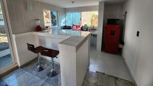 Une cuisine moderne avec un îlot central, des tabourets de bar, un réfrigérateur rouge et une fenêtre donnant sur l’extérieur.