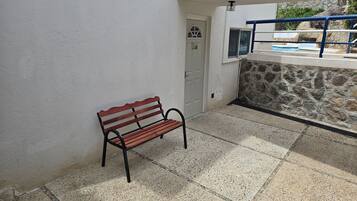 A bench against a white wall, a stone wall, and a pool area.
