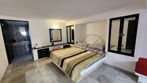 Une chambre à coucher avec un lit, une coiffeuse avec un miroir, une porte donnant sur une salle de bain et un grand miroir sur le mur.