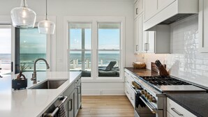 Una cucina moderna con un'isola grande, elettrodomestici in acciaio inossidabile e vista sull'oceano attraverso ampie finestre.