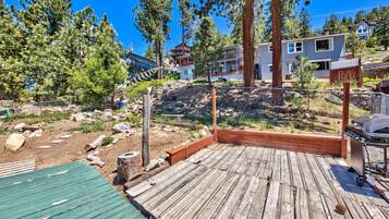 A wooden deck with a barbecue grill, surrounded by trees and a rocky landscape.