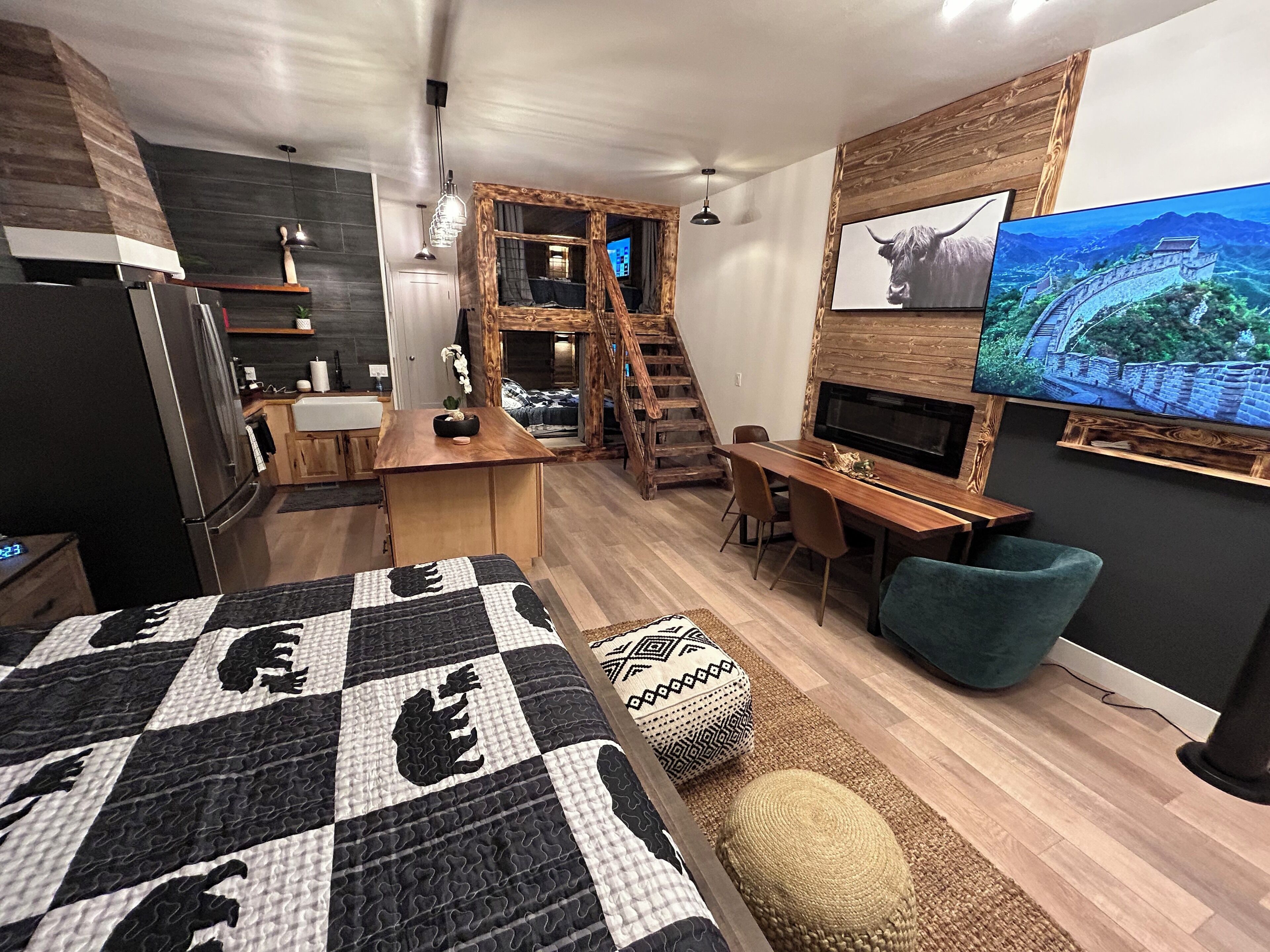 A modern bedroom with a large bed, a desk, a TV, and a staircase leading to a loft.