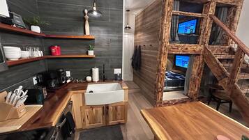 A modern kitchen with dark tiles, wooden shelves, and a wooden staircase.