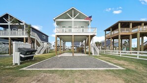 Ein strandnahes Anwesen mit mehreren Ebenen, darunter ein Balkon mit einer US-amerikanischen Flagge, ein überdachter Bereich mit Grill und ein Holzterrasse.