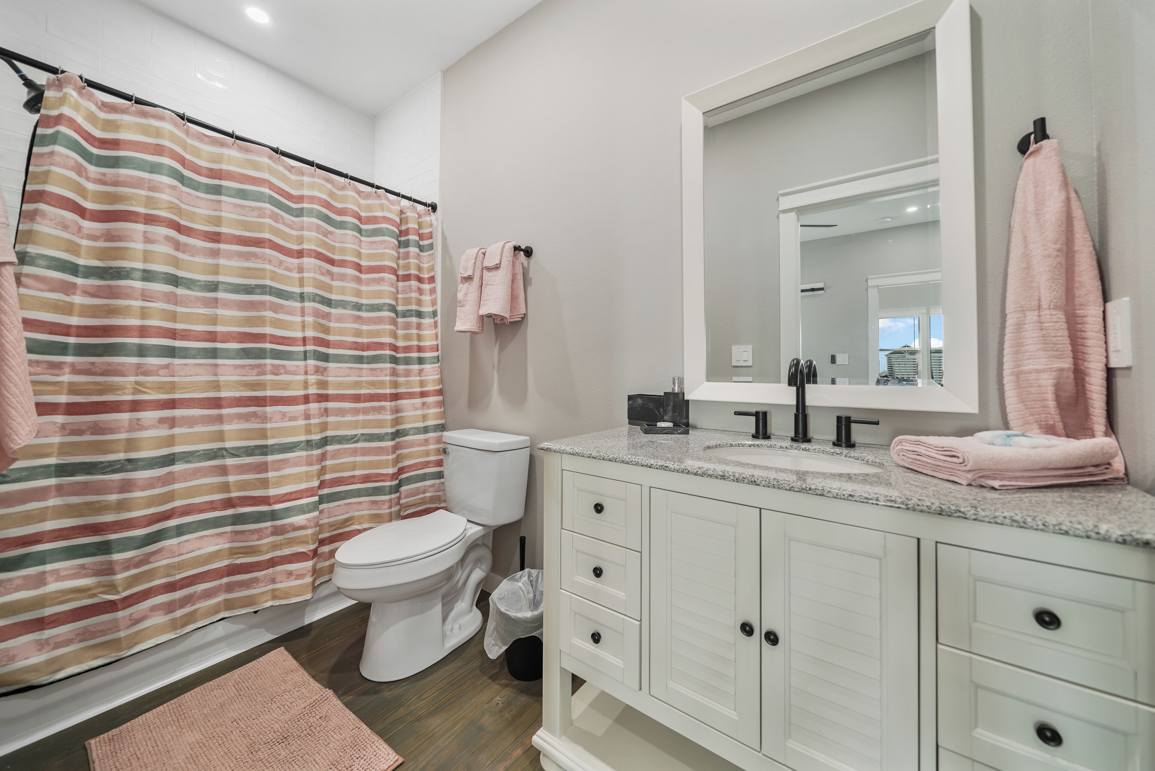A bathroom with a striped shower curtain, a toilet, a sink with a mirror, and a white vanity.