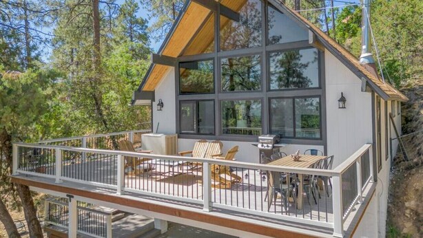 Eine moderne Hütte mit einer Terrasse, großen Fenstern und einem Schornstein.