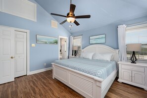 A bedroom with a bed, a ceiling fan, a nightstand, a window with curtains, and a door.